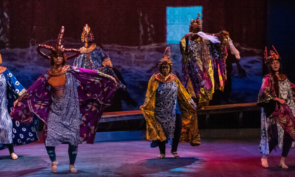 People in brightly colored, patterned costumes and textiles dance onstage.