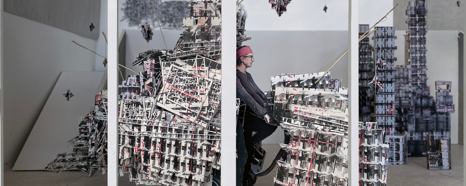 Installation art exhibition seen through a gallery window with bicycle, training wheels, laser cut packing boxes.