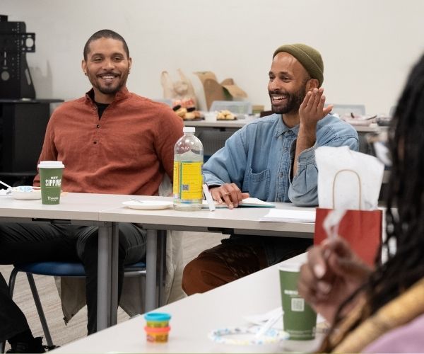 Two men of color sit at conference tables speaking and laughing.