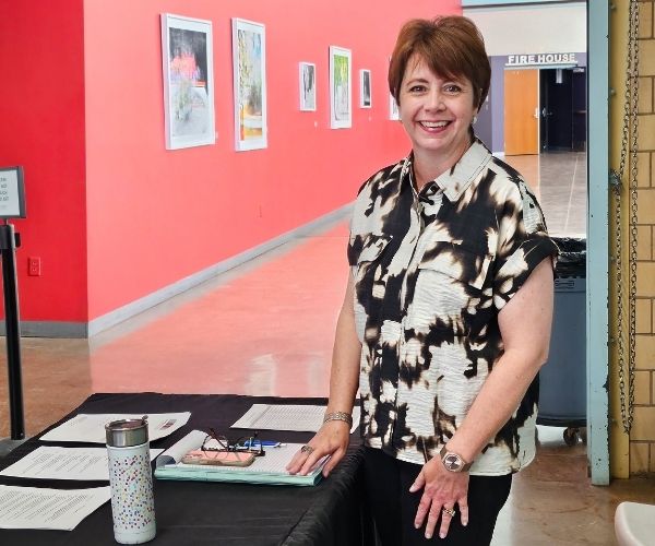 A woman with a black and white blouse stands outside of a gallery with red walls