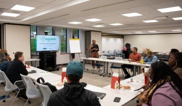 A classroom in a U-shaped seating format with a discussion and woman of color facilitating.