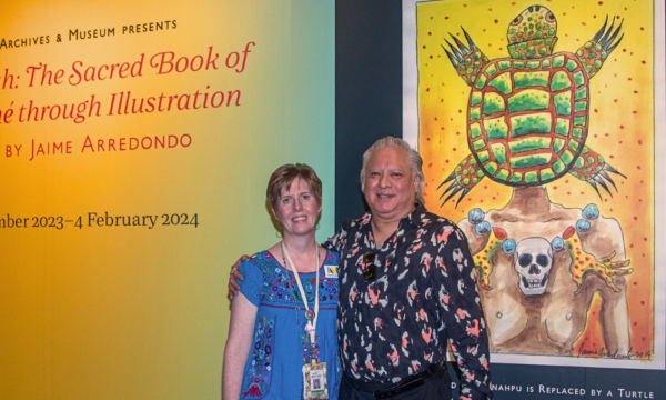 Man and woman stand together in front of an exhibition entrance with a large wall and colorful image behind them.