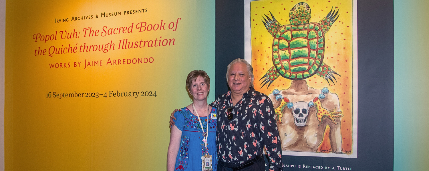 Man and woman stand together in front of an exhibition entrance with a large wall and colorful image behind them.