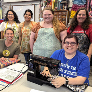 Class participants gather around a sewing machine for a group photo.