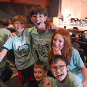 A group of smiling students huddle together for a photo in the audience seating of a theatre.