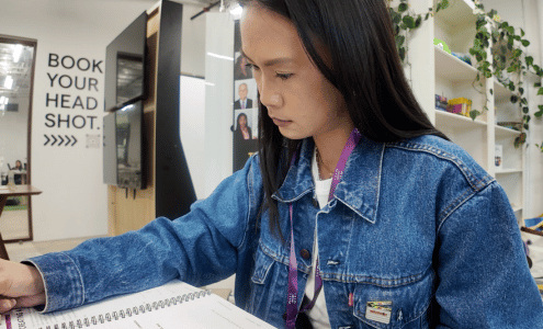 Woman in jean jacket sits at desk during a workshop program writing in a notebook.