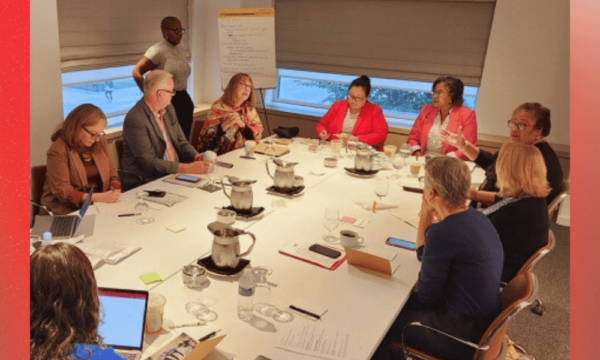 A group of people sit around a board room table talking and smiling.