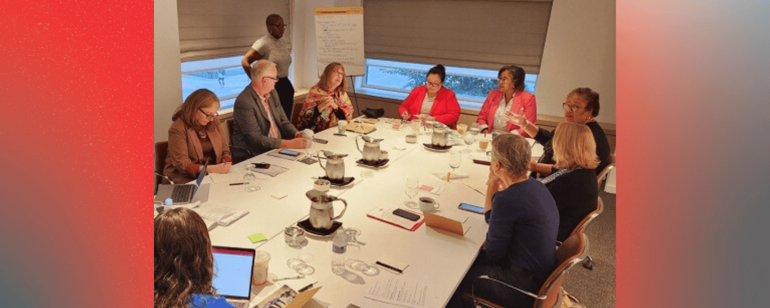 A group of people sit around a board room table talking and smiling.