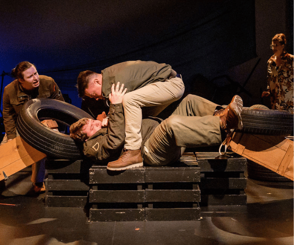 A man leans over another man seeing if he is alive in a dramatic moment during a theatre play.