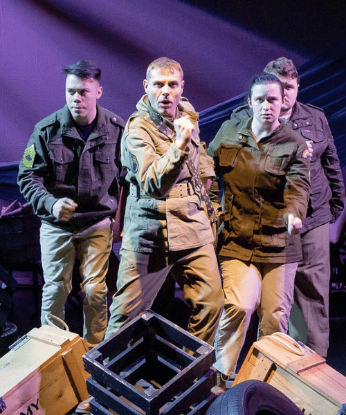 Men and women in military uniform onstage in a theatre production.