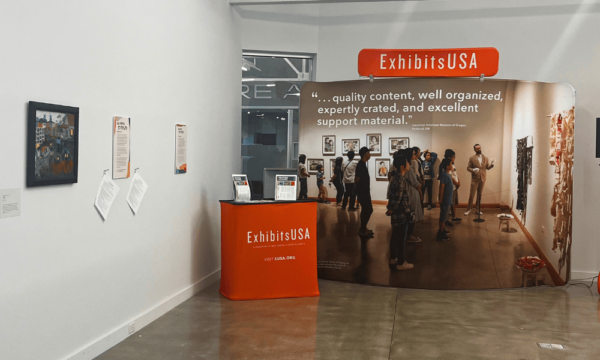 A banner stand that says ExhibitsUSA along with artwork on a gallery wall.