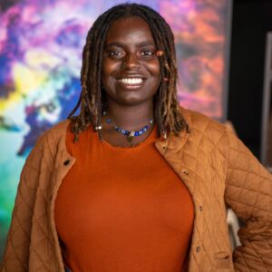 Alagia McKizia portrait with orange shirt and cardigan with colorful background.