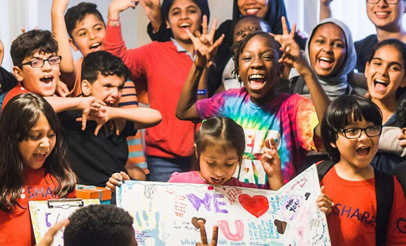 Boys and girls laughing and jumping holding a decorated poster.