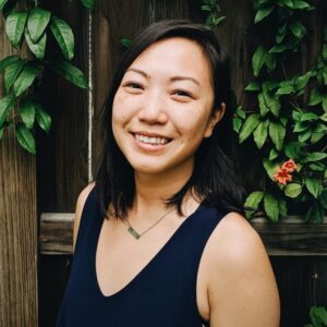 Vietnamese American woman smiling wearing a black shirt in front of greenery.