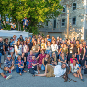 A large group of people outdoors with some standing on a small food truck in the background. Everyone is smiling in fun poses.