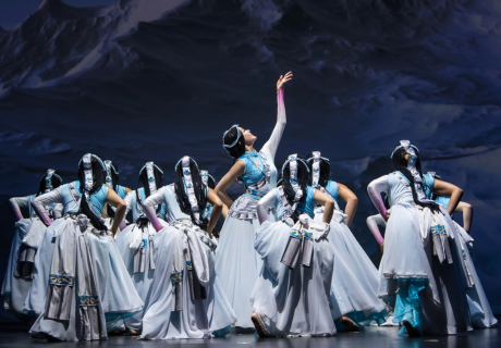 Women in long blue dresses dance onstage.