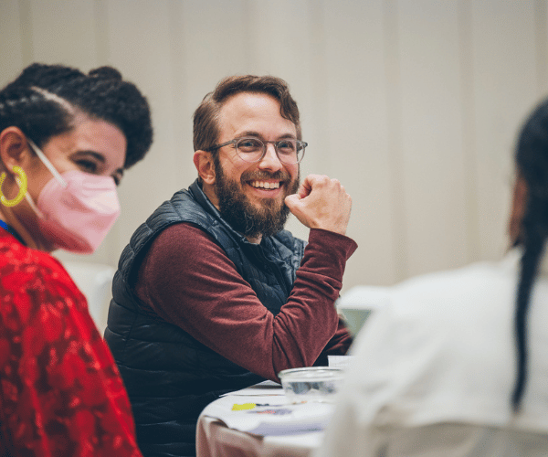 Three artists sit at a table with pens and papers and are all smiling.