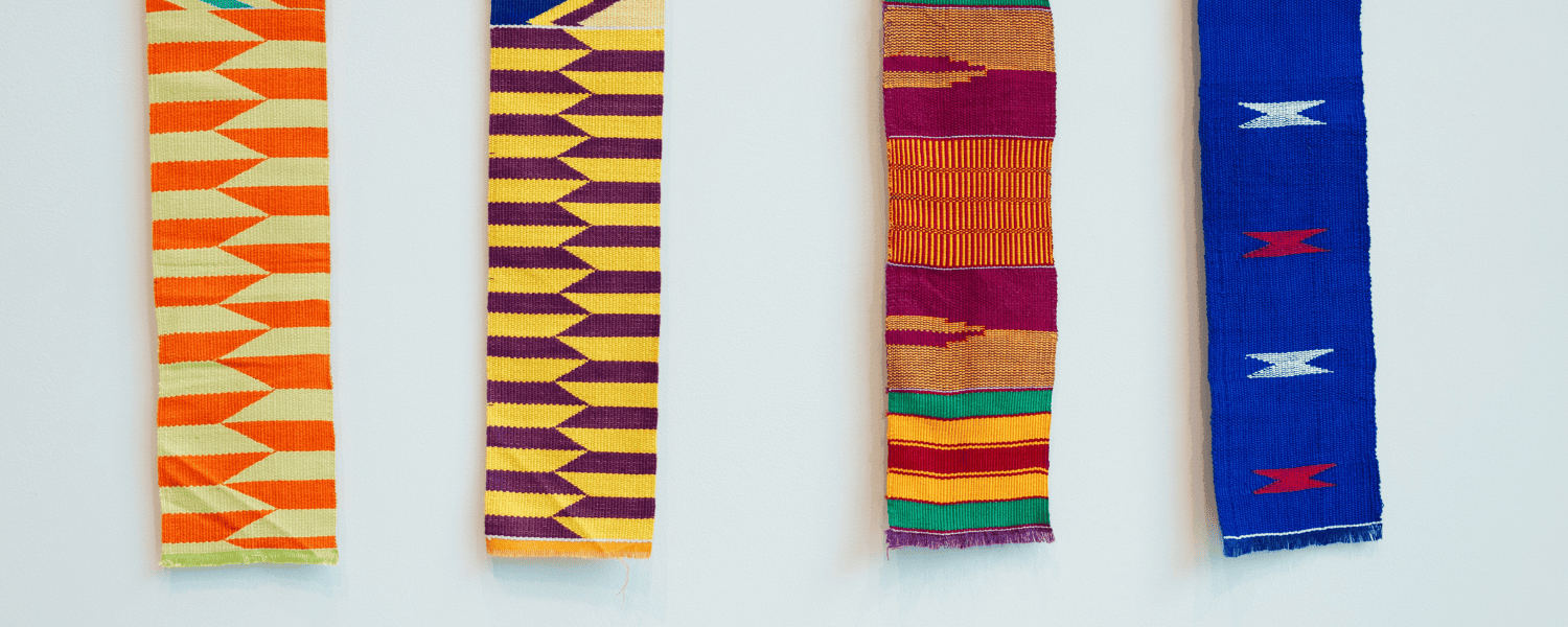 Four Kente cloths each with different patterns and colors. From left, orange with yellow, yellow with dark red, red, orange with green, and last on the right, blue with white and red.